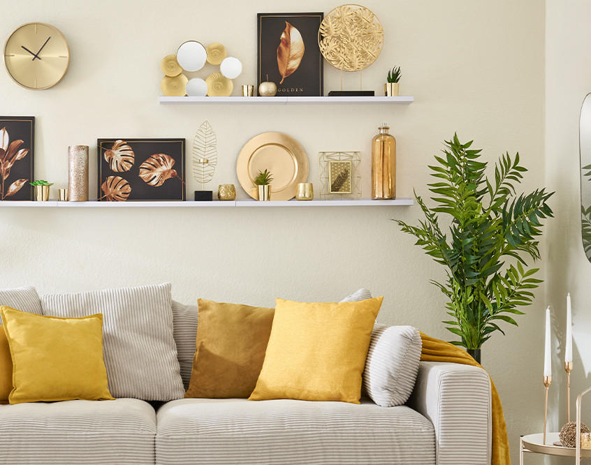 Wohnzimmerdeko in Gold und Grün. Graues Sofa mit gelben Kissen, Wandregale mit Bildern, Pflanzen und Accessoires.