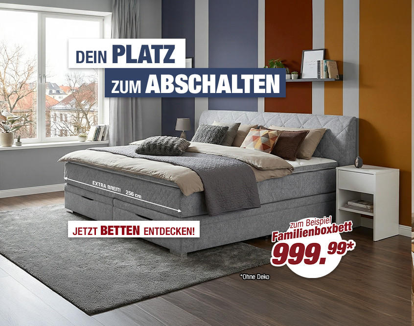 Modernes Schlafzimmer mit großem gepolstertem Boxspringbett, grauem Teppich und Nachttisch vor Fenster mit Blick auf Stadt