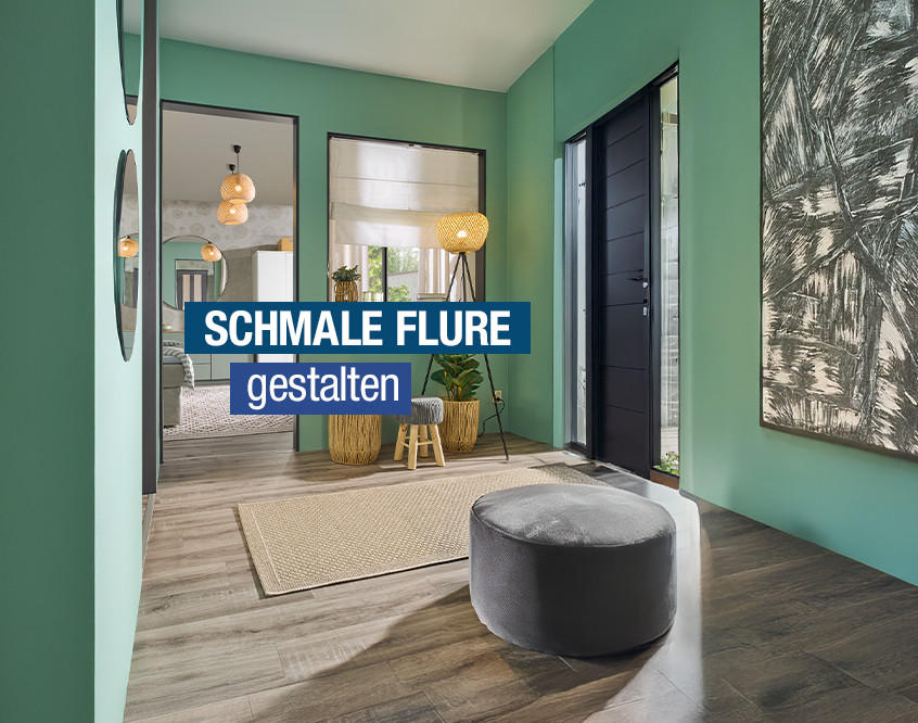 Schmaler Flur mit grün gestrichenen Wänden, großem abstraktem Wandbild, grauem Sitzpouf und Stehlampe neben schwarzer Eingangstür