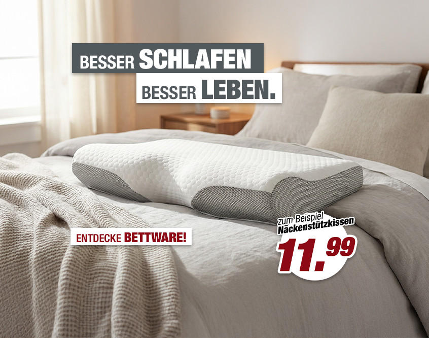 Bett mit mehreren Kissen und grob gestrickter Decke vor hellem Fenster mit Vorhängen