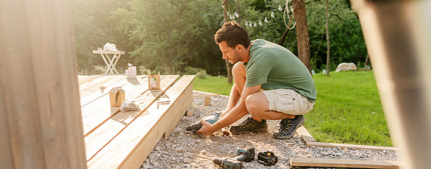 Mann kniet auf Kies und arbeitet an einer Holzterrasse im Garten