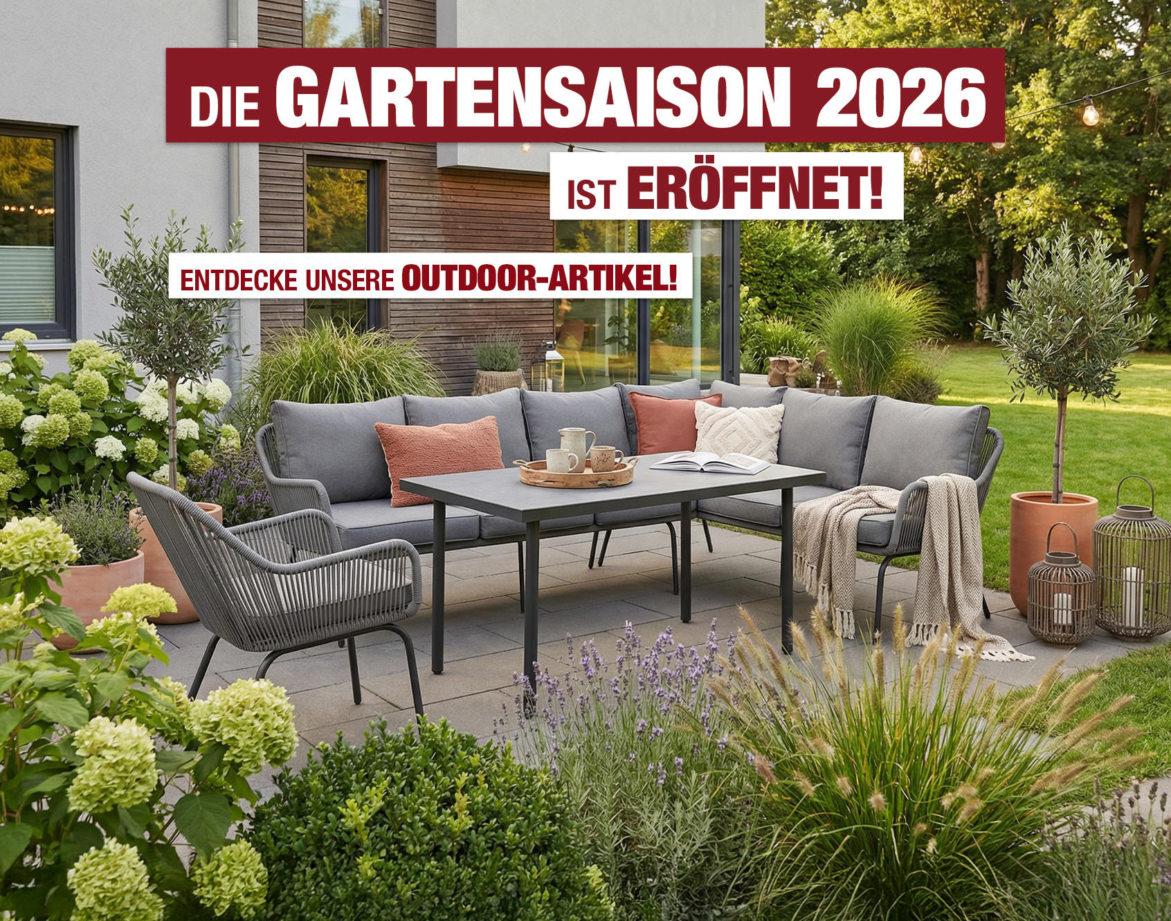 Terrasse mit grauem Sofa, Stuhl, Tisch und Kissen vor Haus mit Gartenpflanzen
